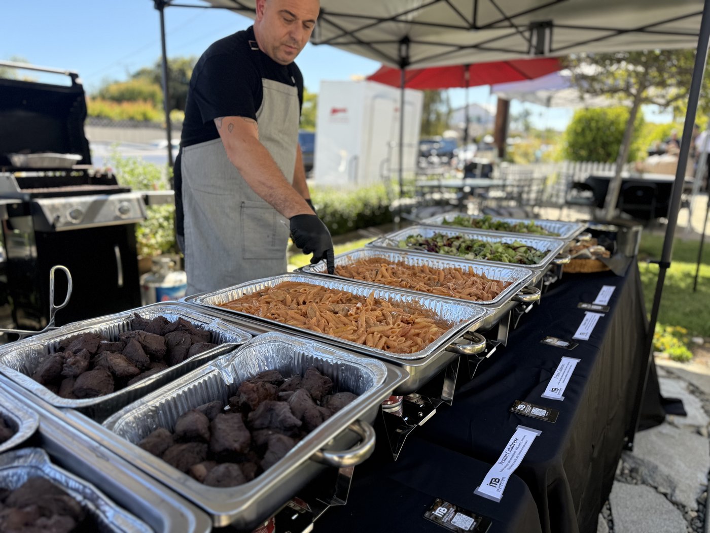 Italian Brothers chef preparing to serve an outdoor buffet of pasta, meat and salads
