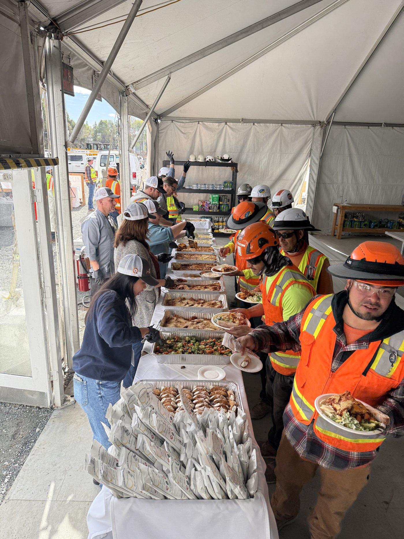Catering team serving construction workers along a buffet inside an event tent